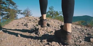 在山崖上徒步旅行的女旅行者的脚上的观点。慢动作