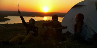 年轻的朋友有乐趣与火花和歌曲与吉他在日落户外