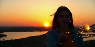 夕阳西下时，一名年轻女子手持荧光棒站在小山上