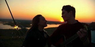 年轻幸福的夫妇一起玩火花唱歌与吉他在户外日落