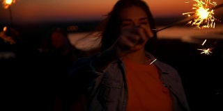 夏日日落时，快乐的年轻女子在小山上玩烟火