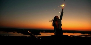 年轻女子举起手与闪光在惊人的日落在山上