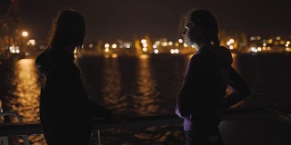 两个迷人的年轻女人的剪影在夜里在船上旅行。船上的闺蜜