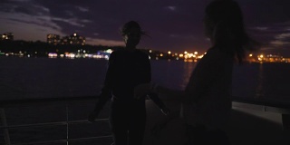 夜晚，两个美丽的年轻女子在甲板上跳舞的剪影。船上的闺蜜