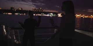 夜晚，两个美丽的年轻女子在甲板上跳舞的剪影。船上的闺蜜