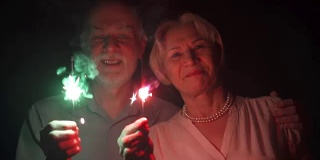 缓慢的运动。一对老年夫妇拿着烟花庆祝圣诞节。幸福全家手捧孟加拉灯
