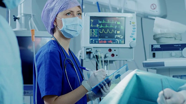 在医院的手术室里，麻醉师注视、监测和控制病人的生命体征，并向主刀医生点头示意继续手术。