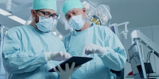 两名专业外科医生站在现代医院手术室里使用数字平板电脑。