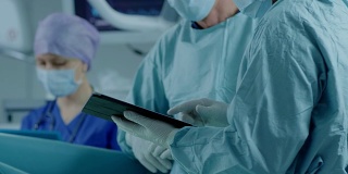 两名专业外科医生站在现代医院手术室里使用数字平板电脑。