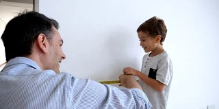 可爱的小男孩在爸爸的帮助下学习如何测量墙壁和使用卷尺