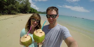 自拍:年轻的旅行者把椰子举到镜头前，抿了一口
