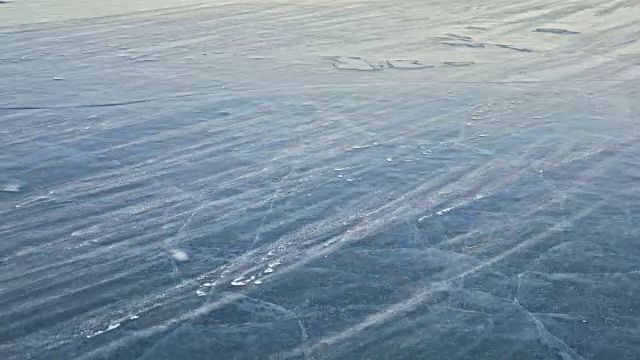 雪在冰面上飞舞。雪花在贝加尔湖的冰面上飞舞。冰非常美丽，有独特的裂缝。雪花闪耀着红光。在日落时分。高对比度。