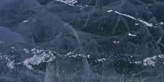 雪在冰面上飞舞。雪花在贝加尔湖的冰面上飞舞。冰非常美丽，有独特的裂缝。雪花闪耀着红光。在日落时分。高对比度。