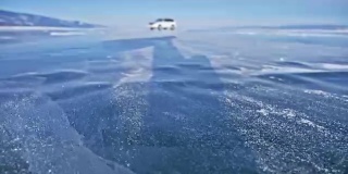 雪在冰面上飞舞。雪花在贝加尔湖的冰面上飞舞。冰非常美丽，有独特的裂缝。背景视图山景。雪花闪耀着红光。