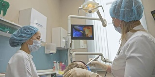 医生使用特殊的口腔内检查数码微型相机对牙齿进行检查。在监视器上，牙医和病人可以看到牙齿、牙齿问题的视频。牙医在现代牙科诊所里治疗病人。