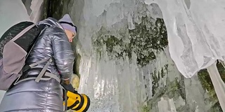 贝加尔湖冰洞上的女游客。冬岛之旅。女孩背包客正在冰洞中行走。游客看着美丽的冰洞。徒步旅行者穿银色夹克，背包，led灯。