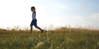 在阳光明媚的日子里，小男孩举起双手在草地上奔跑。孩子在草坪上慢跑。快乐的微笑的男孩有乐趣在一个夏天的草地上的自然。慢镜头