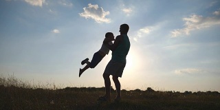 夏天，父亲在草地上纺着他的小儿子。爸爸让婴儿在大自然中转圈。日落时分，一家人在操场上玩耍。爸爸和孩子在一起玩。特写慢动作