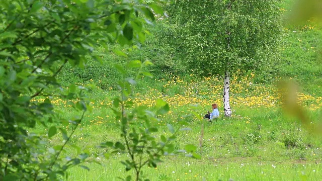 一个女人坐在桦树附近的草地上，在花丛中休息。他起身离开了。