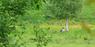 一个女人坐在桦树附近的草地上，在花丛中休息。他起身离开了。