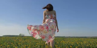 一个女人穿着随风飘动的裙子走在盛开的黄色田野上
