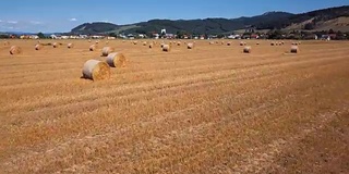 在有圆草堆的田野上空低空飞行。风景如画的小村庄和山峦为背景。