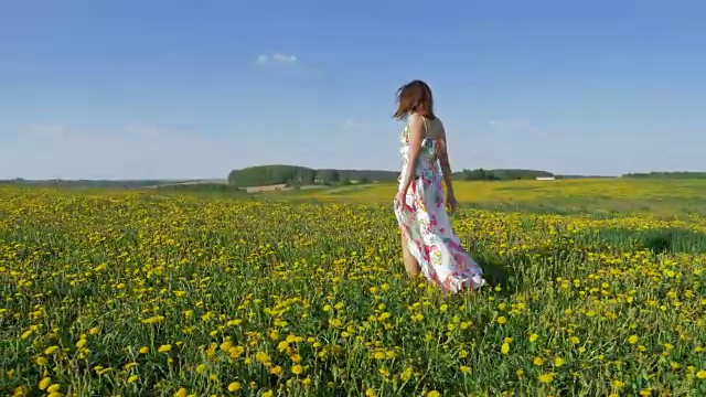快乐的女人走在盛开的黄色田野上，穿着随风飘动的裙子