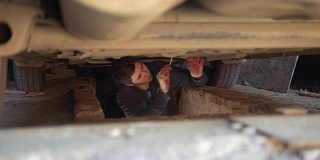 一个年轻人在车下面从托盘下面拧出细节