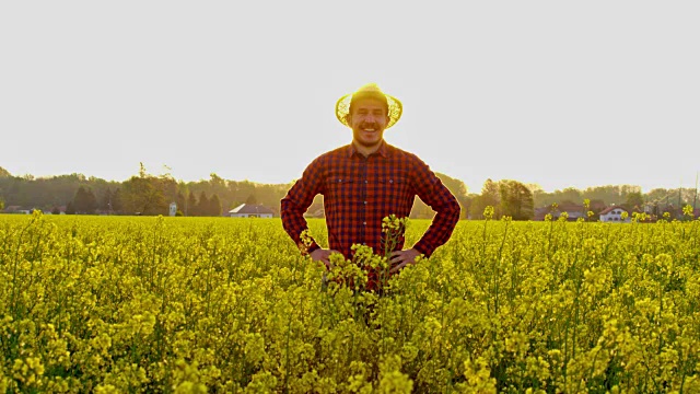 肖像顽皮的农民跳出阳光，田园诗般的黄色油菜田，慢镜头