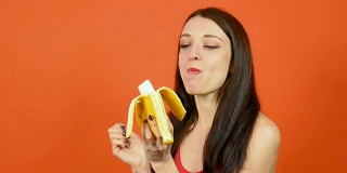 年轻健康的女人完美的皮肤吃香蕉明亮的橙色背景。热带水果。素食主义者的饮食概念