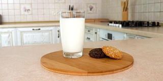 近距离的一杯牛奶与健康的家庭制作的多种谷类饼干。以白色厨房为背景的旋转相机。Dolly-shot。