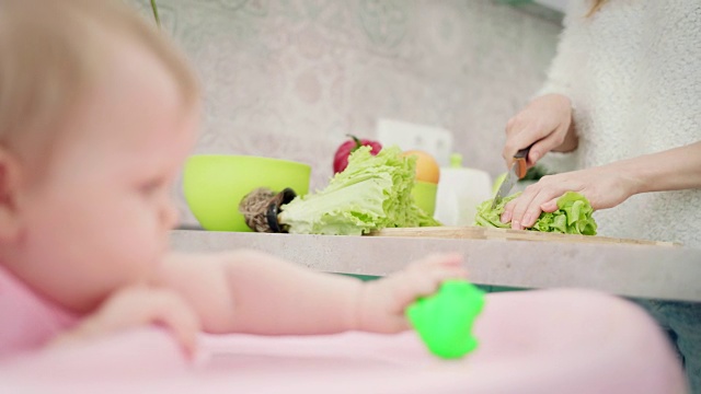 妈妈在给宝宝做饭。妈妈正在切绿色沙拉。女性烹饪健康食品