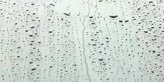 阳光下的雨点或水滴在玻璃上流动。特写雨落溅在明亮的表面的镜子的汽车背景