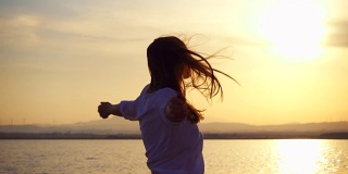 日落时，年轻女子在湖面上旋转的剪影。在黄金时刻，慢动作的女子舞蹈