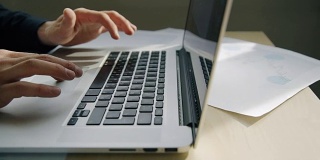 在现代化的室内环境中，年轻的商人用笔记本电脑坐在办公桌前打字