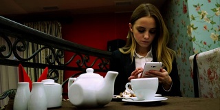 年轻女孩在咖啡馆边喝茶边用智能手机