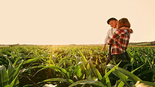 女农民和儿子站在阳光明媚、田园诗般的农村玉米地里，实时拍摄