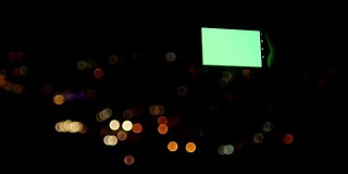 绿色屏幕的智能手机和散景圈灯光背景的城市