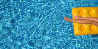 俯视图美丽的晒黑的女孩在太阳镜和粉红色的比基尼躺在黄色的充气床垫在游泳池。年轻女子放松在盆地的酒店在夏季旅游。假期的概念。近距离