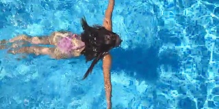 年轻美丽的女孩在粉红色比基尼漂浮在酒店的游泳池。在一个阳光明媚的日子里，一个不可辨认的棕色头发的女人在清澈的蓝色水池里游泳。暑假或假期的概念。俯视图特写