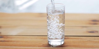 水从瓶子倒进木桌上的玻璃杯里