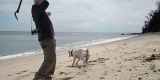 一个年轻人在海滩上和他的狗玩耍。从背后开枪