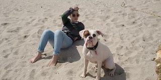 一个可爱的白人女人和她的白色拳击狗在沙滩上放松的慢动作