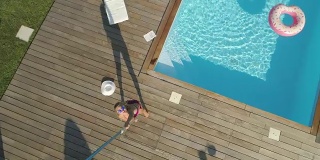 AERIAL, POV:年轻女子在泳池边放松，开始向无人机扔东西。