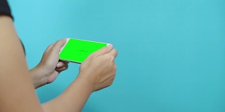 一名女性在蓝色桌面上使用绿色屏幕的智能手机。女性的手滚动页面，轻触触摸屏。