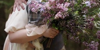 年轻夫妇新娘新郎拥抱近绿色森林散焦背景慢镜头野花花束。男人潮人抱着拥抱女人浪漫的约会情绪亲密的关系婚礼