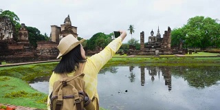 慢镜头亚洲女游客在泰国素可泰历史公园古塔寺庙泰国建筑前自拍。女性旅行者在休闲泰国服装风格访问城市概念。