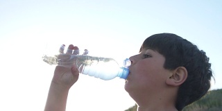 在晴朗的天空中，男孩正在喝塑料瓶里的水