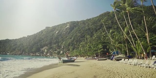 移动拍摄在一个田园诗般的海滩与海浪和大海，在岸边的船只和在背景山与绿色的丛林。