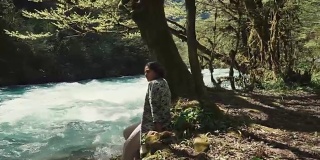 一个孤独的少女坐在林地的地上，看着小溪